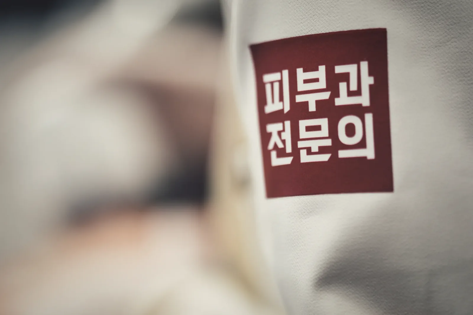 흰 가운 소매에 붙은 '피부과 전문의' 자수 패치 클로즈업