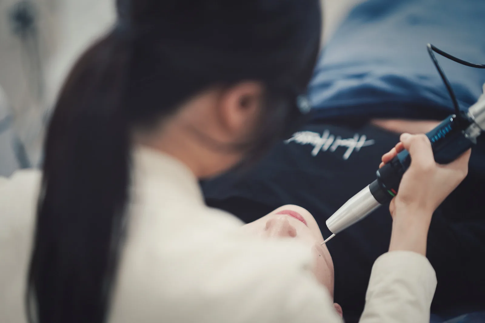 시술 베드에 누운 고객의 얼굴에 레이저 핸드피스를 대고 집중해 시술하는 힐하우스피부과 의료진